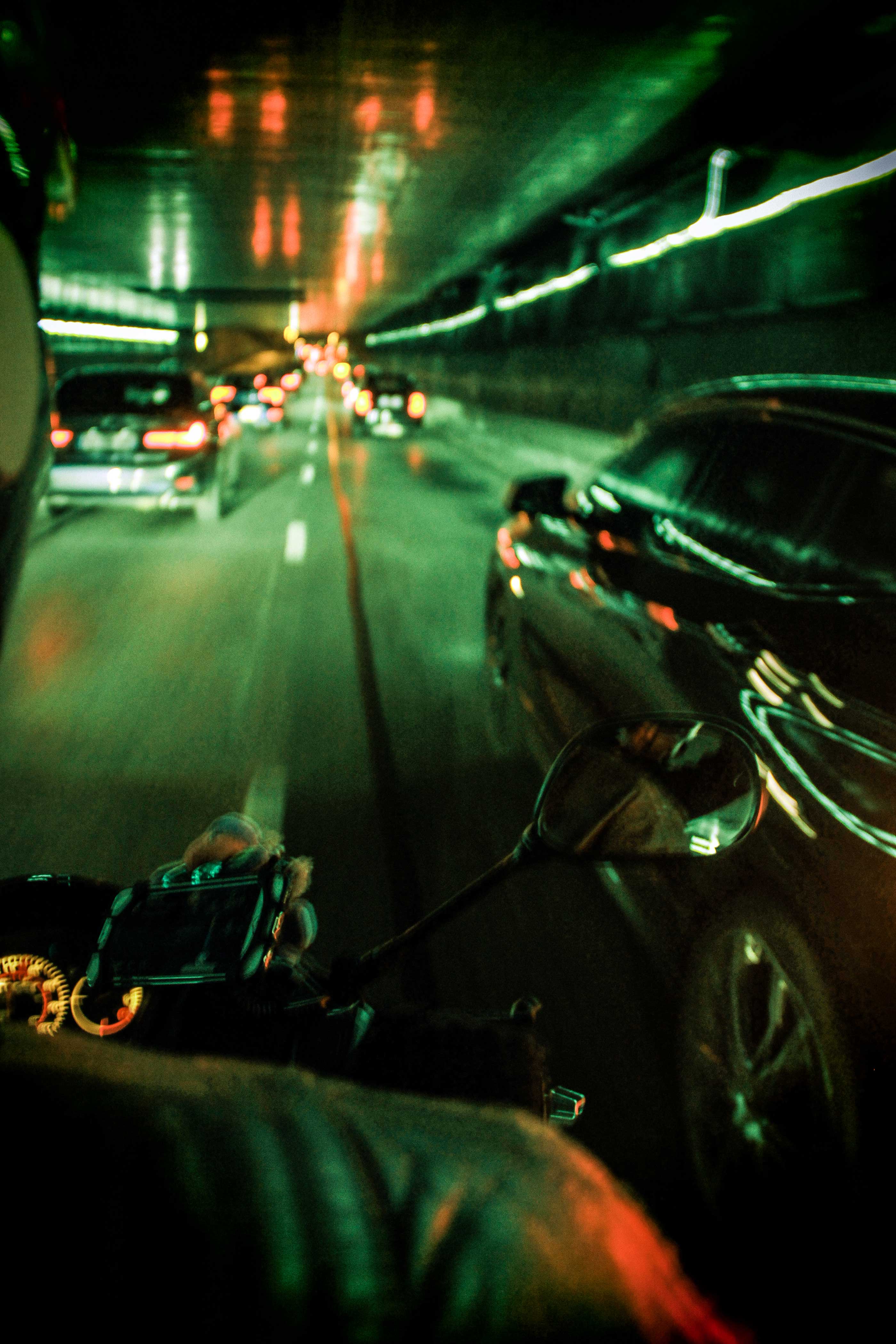 photo of someone on a scooter riding at night under a tunnel with green lights